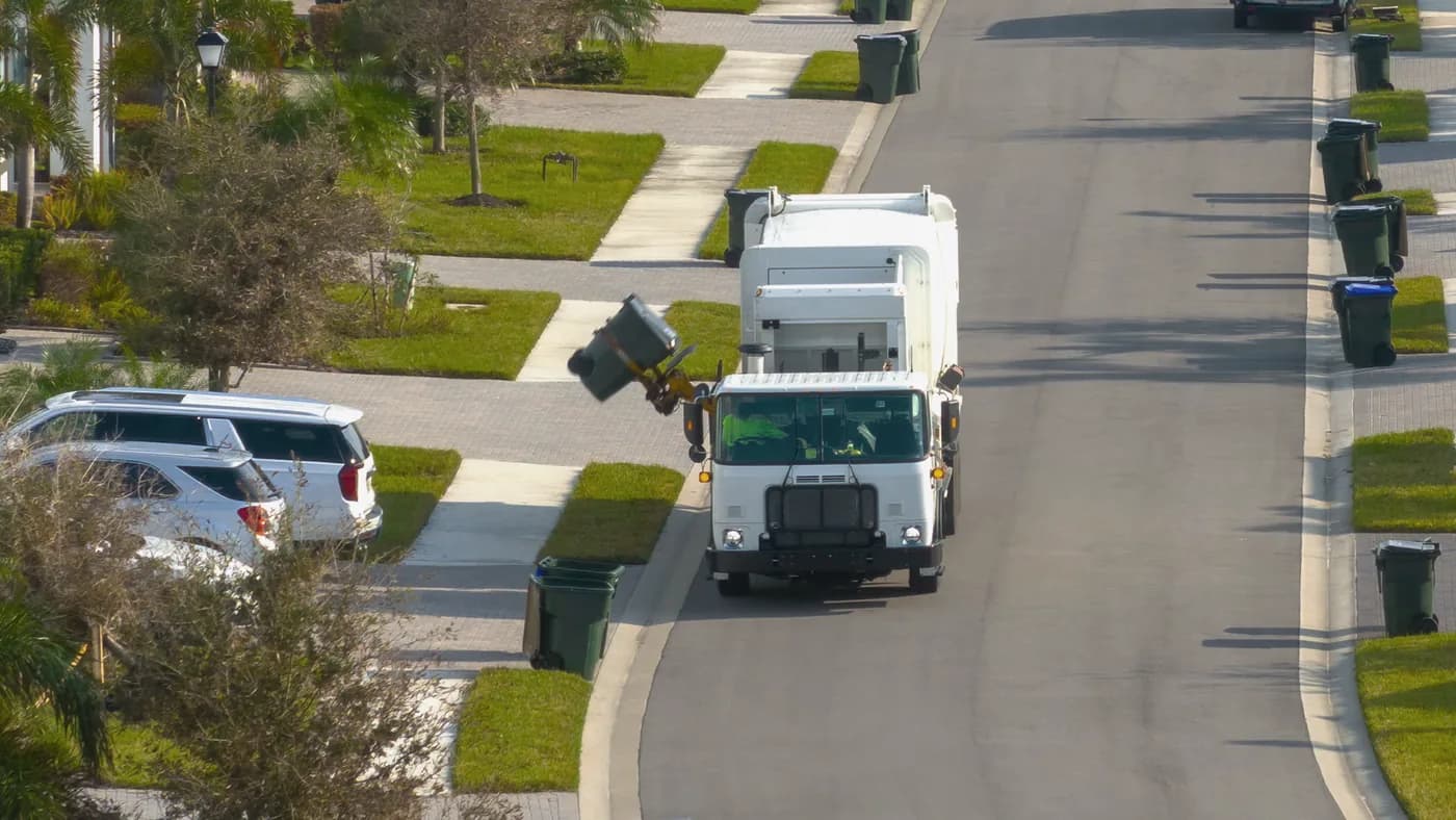 Automated side-loader waste truck lifting a cart on a residential street
